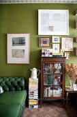Green Chesterfield sofa, antique display case and pictures on green wall