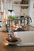 Blick auf Küchentheke mit eingebautem Spülbecken und Vintage Armatur, im Hintergrund brennende Kerzen neben Schale mit Knoblauchknollen