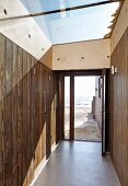 Hausflur mit Einbauschrank aus Holz und grossflächiges Glasdach, Blick durch offene Haustür auf Sandstrand und Meer