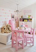 Pink children's table and soft toys in front of heart-patterned wallpaper