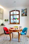 Brightly coloured, retro, upholstered chairs around antique, exotic-wood table below colourful, spherical pendant lamps in open-plan kitchen