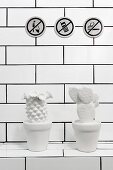 Three prohibitory pictograms on tiled wall and white cactus ornaments on masonry shelf