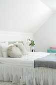 Stacks of scatter cushions in various shades of white and grey on box-spring bed in attic bedroom