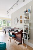 White ladder shelves next to piano and classic chair against grey-painted wall; lighting strip with spotlights and dining area in background