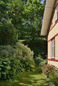 Sonnenbeschienene Fassade eines Holzhauses mit grünem Garten am Waldrand