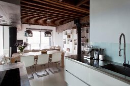 Blick von Küche auf Essplatz unter spiegelnden Kugellampen an rustikaler Holzdecke in Loftwohnung