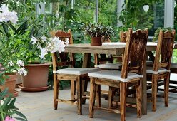 Tisch und Stühle aus Massivholz, seitlich und im Hintergrund Pflanzentöpfe im Wintergarten
