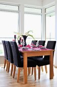 Black-upholstered chairs around set table in front of floor-to-ceiling windows
