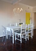 White dining table, refurbished second-hand chairs and Ghost chair below chandelier