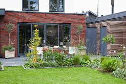 View from garden over flowering plants in beds and on terrace to modern, brick extension
