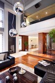 Pendelleuchten mit Kugelschirm in verschiedener Höhe über Bodentisch aus Makassar Holz und schwarze Ledersofagarnitur in elegantem Wohnraum mit Galerie