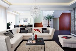 Elegante, helle Couch übereck und Couchtisch auf flokatiartigem Teppich in offenem Wohnraum mit indirekter Deckenbeleuchtung