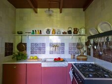 Kitchen counter with dusky-pink base units below shelf of jugs on tiled wall