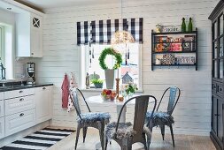 Gemütliche, skandinavische Küche mit Schwarzweiss-Kontrasten, zentraler Tisch mit Vintagestühlen, Textilien mit Karo und Blockstreifen