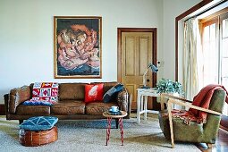 Cushion on pouffe in front of traditional brown leather sofa and fifties-style armchair in eclectic living room