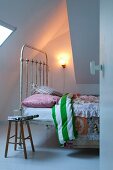 Vintage metal bed, rustic wooden stool and simple sconce lamp next to sloping ceiling section