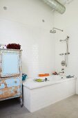 Bathtub and vintage cupboard with peeling paint in bathroom with white wall tiles