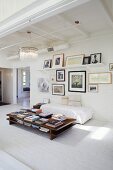 Stacks of books on low coffee table, simple couch with white cover on whitewashed brick floor and gallery of pictures on wall