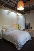 Double bed with ruffled bedspread in simple room with wicker pendant lampshade hung from corrugated metal ceiling