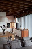 Comfortable grey sofa in front of kitchen-dining area with free-standing counter in elegant, renovated loft apartment with rustic, wood-beamed ceiling