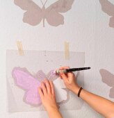 Hand-crafted butterfly stencil used as template for painting pattern on wall - woman's hands holding paintbrush