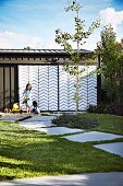 Children playing in sandpit in front of garage with steel and plexiglas sliding doors with zigzag patterns in summery garden