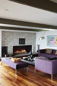 Elegant, purple sofa set in lounge area with arc lamp and cosy open fire in stone wall