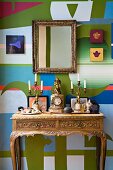 Antique mantel clock flanked by candlesticks on Baroque console table and gilt-framed mirror on artistically painted wall