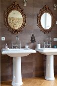 Zwei Standwaschbecken vor gefliester Wand und Spiegel in verzierten Goldrahmen