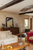 Low coffee table on castors in front of pale sofa and sideboard against stone wall in open-plan interior of renovated country house
