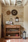 Console table with turned legs, shelves and carved drawer fronts below collection of vintage-style clocks on stone wall