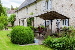 Terrace with metal pergola in garden adjoining stone country house