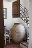 Old amphora for storing olives in niche below winding country-house staircase with wrought iron balustrade