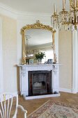 Mirror with magnificent gilt frame above open fireplace in elegant interior with crystal chandelier