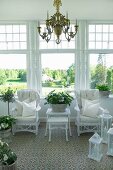 Chandelier above white, wicker chairs, set of matching tables and lanterns in conservatory with view into sunny park