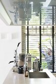 Freistehende Kücheninsel mit Spülbecken, Espressomaschine, oberhalb Dunstabzugshaube, im Hintergrund Fenster mit Jalousie