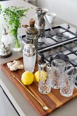Wooden tray of glasses and cocktail equipment next to gas hob on wooden counter