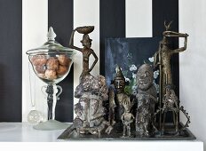 Collection of metal ethnic figurines and glass jar against wallpaper with wide black and white stripes