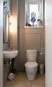 White toilet against grey panelled wall below window; sink below framed mirror with modern strip light