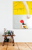Home bar on fifties-style serving trolley below large modern painting on wall