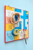 Pin board made from board game collage with gaming pieces used as hooks for scissors, twine and sticky tape