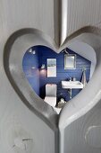 Heart-shaped cut-out in grey wooden door with view into bathroom with blue-painted walls