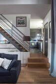 Blick vom eleganten Wohnbereich auf Stahltreppe mit Holzstufen, im Hintergrund graue Hochglanz-Einbauküche