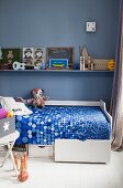White bed with drawers in boy's bedroom with vintage-style toys and blue wall