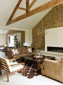 Armchairs and sofa in shades of brown in front of open fireplace in white chimney breast on brick wall