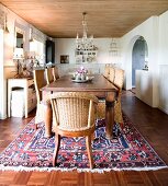 Solid wooden table and wicker chairs on Oriental rug in rustic dining room