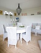 White wicker chairs at round table below vintage pendant lamp in corner of white, wood-clad dining room