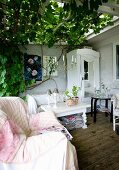 Comfortable armchair with blanket, coffee table and white-painted cabinet on veranda with climber-covered pergola
