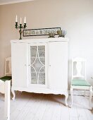 Half-height rustic cabinet painted white flanked by white chairs, all with curved legs