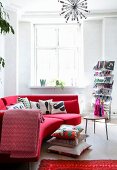 Rotes Designersofa mit Kissenstapel am Boden, Zeitschriftenständer und Beistelltisch mit Retroflair in renovierter Altbauwohnung